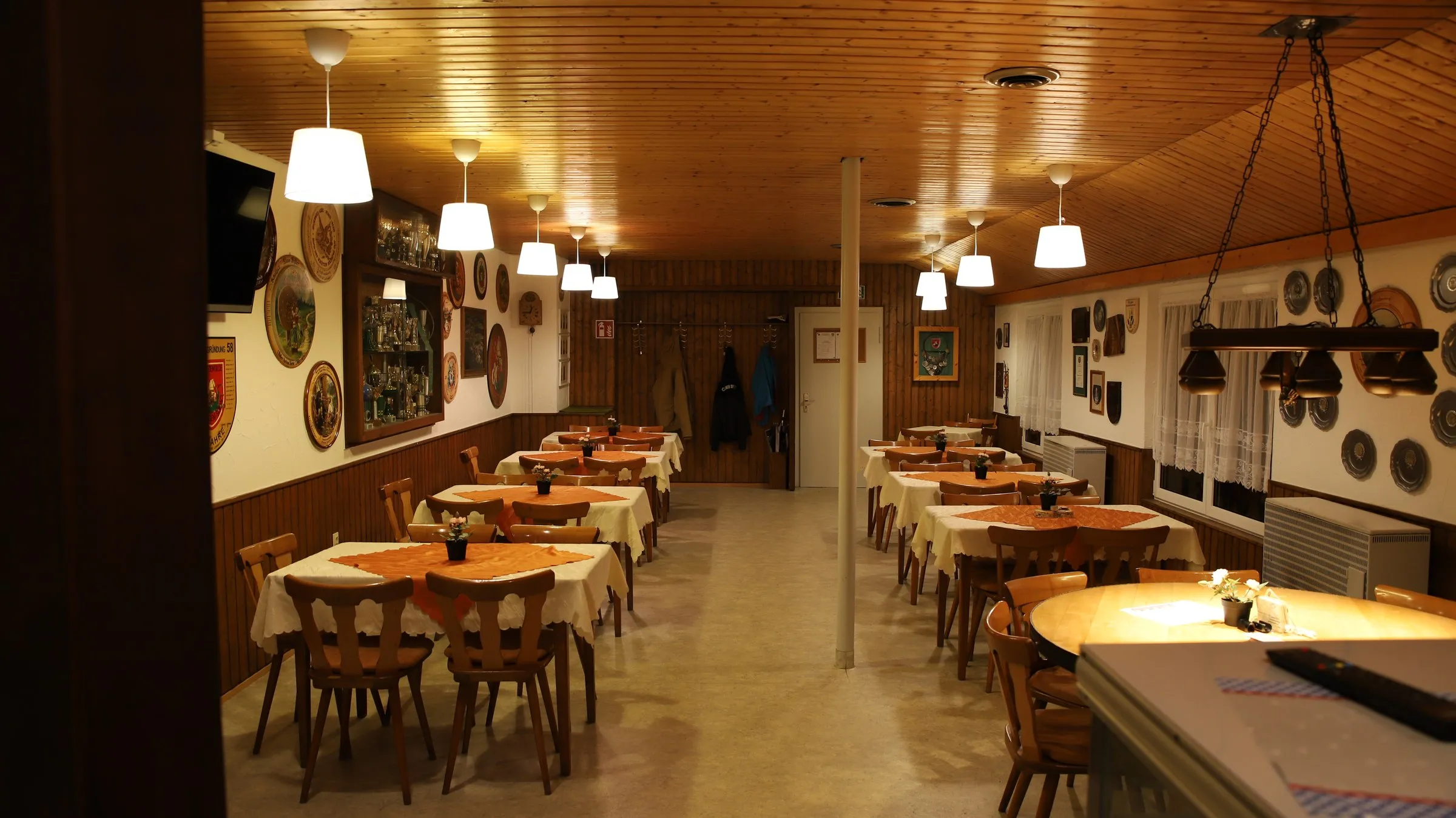 Der Gastraum des Vereinsheims: Holztische mit Stühlen, getäfelte Wände und Fenster zur Terrasse.